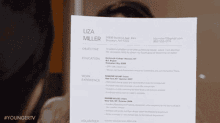 a woman holds up a resume with the name liza miller on it