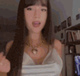 a woman with long hair and a necklace is wearing a white tank top and holding a mask .