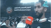a man holding a red pro microphone in front of a saudi professional league logo