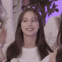 a woman with a bow in her hair is smiling while sitting in front of a group of people .