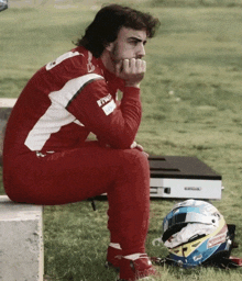 a man sits on a concrete block next to a helmet which says ' alonso ' on it