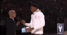 a man in a suit and tie is shaking hands with a basketball player in a white shirt .