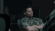 a man in a military uniform is sitting at a table talking to another man .