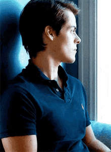a man in a blue polo shirt is sitting on a couch and looking out a window .