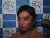 a man wearing headphones is standing in front of a blue and white checkered wall with skulls on it