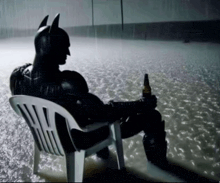 a man in a batman costume is sitting in a chair holding a bottle of beer