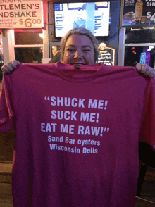 a woman holds up a t-shirt that says " shuck me suck me eat me raw "