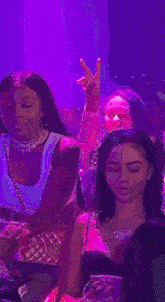 a group of women are sitting at a table in a club . one of the women is giving a peace sign .
