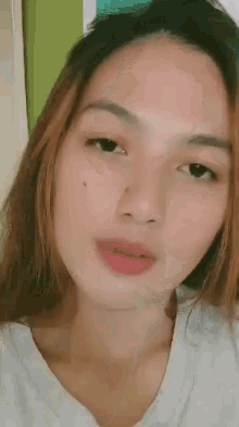 a close up of a woman 's face with a white shirt on and a green background .