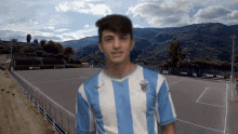 a man wearing a blue and white striped shirt with the letter r on it stands in front of a soccer field