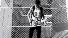 a black and white photo of a man standing behind a chain link fence .