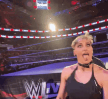 a woman in a black tank top is standing in a wrestling ring with the w logo in the background