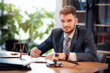 a man in a suit and tie is sitting at a desk with a judge 's gavel and scales of justice