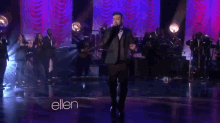 a man in a suit is singing into a microphone on a stage in front of a sign that says ellen