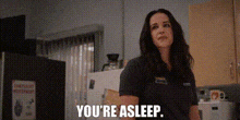 a woman is standing in a kitchen with the words `` you 're asleep '' written above her .