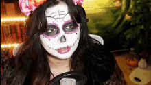 a woman with day of the dead makeup is holding a microphone .