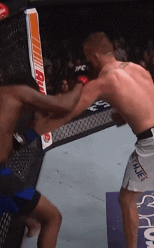 two men are fighting in a cage and one of them is wearing shorts with the word hue on them