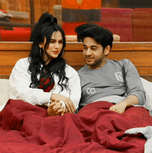 a man and a woman are laying on a bed under a blanket and the man is wearing a shirt that says g