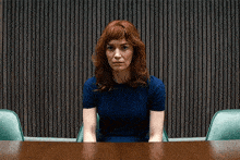 a woman in a blue shirt sits at a wooden table