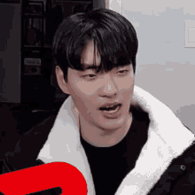 a young man wearing a black shirt and a white jacket is making a funny face with his mouth open .