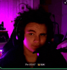 a young man wearing headphones and a microphone is sitting in front of a screen that says the goat