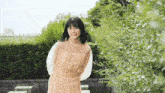 a young woman in a dress is standing in front of a bush and smiling at the camera .