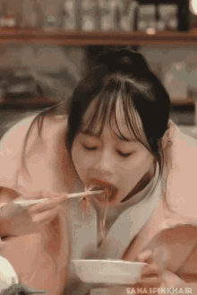 a girl in a pink jacket is eating noodles from a bowl