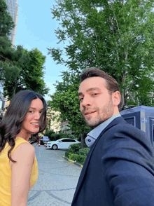 a man in a suit and a woman in a yellow dress pose for a selfie