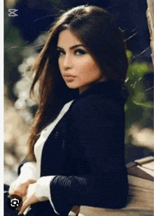 a woman in a black jacket and white sweater is sitting on a bench looking at the camera .