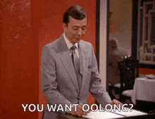 a man in a suit and tie is standing in front of a red wall with the words " you want oolong " written on the screen