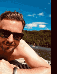 a shirtless man wearing sunglasses is laying on a dock near a body of water