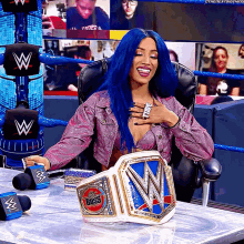 a woman with blue hair is sitting in a chair holding a wrestling belt that says the boss