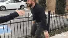 a man with a beard is giving a high five to another man while standing next to a fence .