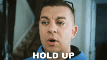 a man in a blue shirt says hold up in white letters