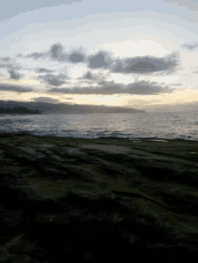 a sunset over a body of water with a grassy hill in the foreground
