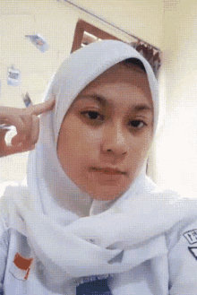 a girl wearing a white hijab and a white shirt has her finger on her ear