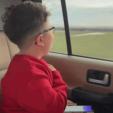a young boy in a red sweater looks out the window of a car