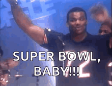 a man in a football jersey is standing in front of a microphone and says super bowl baby !