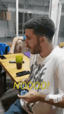 a man sitting at a table with the word nooo written on his shirt
