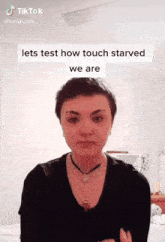 a woman with short hair is wearing a black shirt and a necklace and says lets test how touch starved we are ..