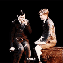 two men are sitting next to each other on a stage and one of them is saying shhh .