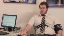 a man in a tie is sitting at a desk with a computer monitor behind him