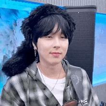 a young man wearing a plaid shirt and a furry hat is looking at the camera .