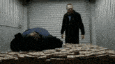 a man is standing next to a pile of money while another man is laying on the floor .