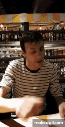 a man in a striped shirt is sitting at a table in a bar