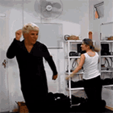 a man and a woman are dancing in a room with a fan on the wall