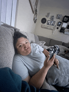 a woman laying on a couch holding a cell phone with j and m written on the wall behind her