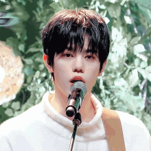 a young man singing into a microphone while wearing a white turtleneck sweater