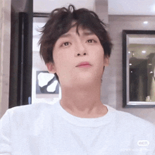 a young man with messy hair is wearing a white t-shirt .