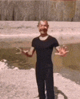 a man in a black shirt and black pants is standing in the sand with his arms outstretched